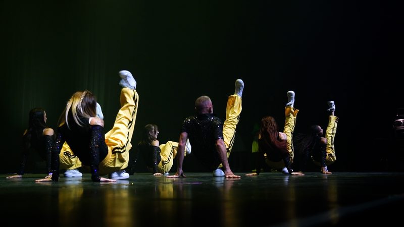 Des danseurs en jaune et noir, au sol, dans une lumière jaune.